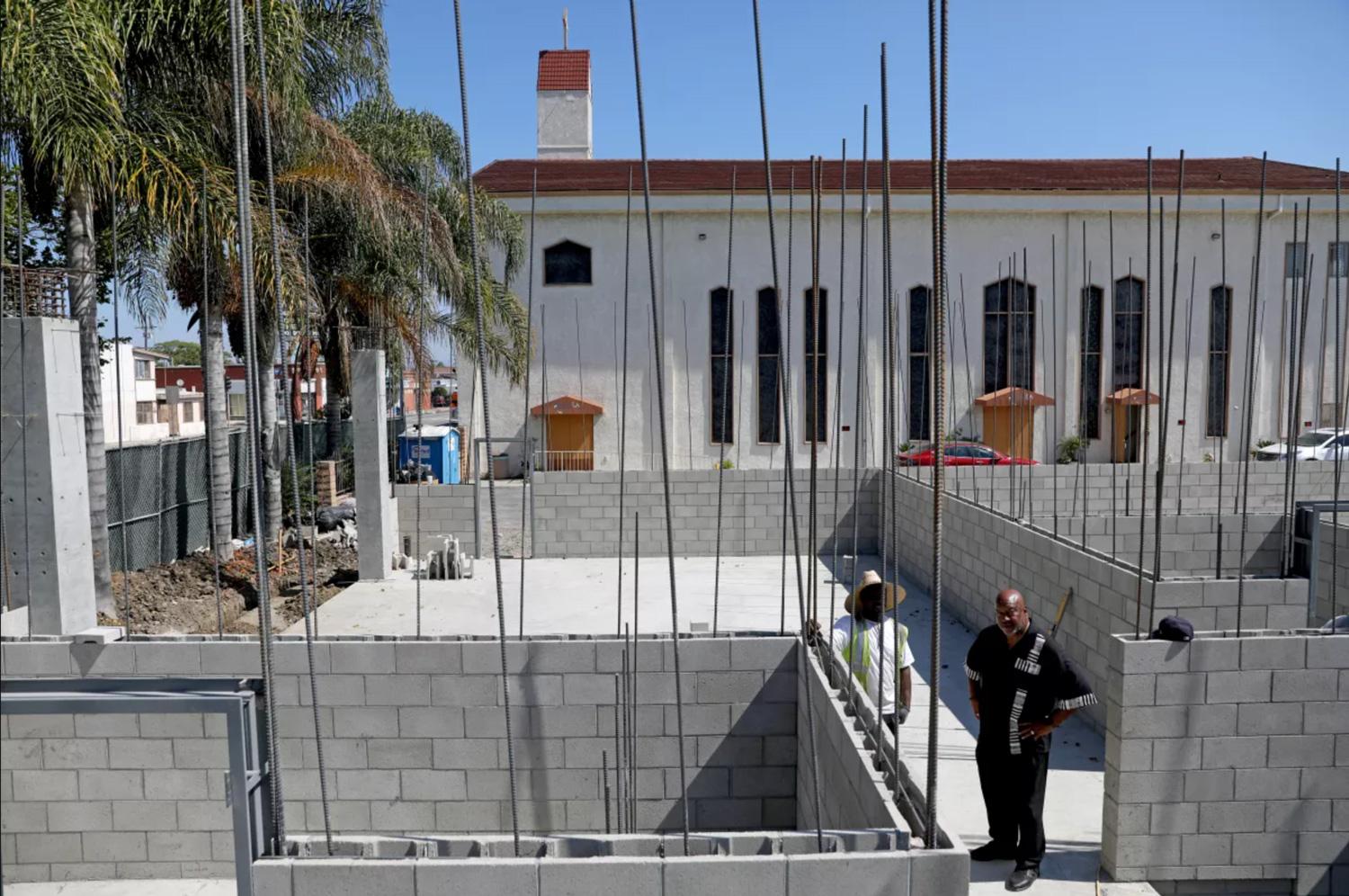 Construction zone with Church building in the background and pastor surveying the job alongside construction worker